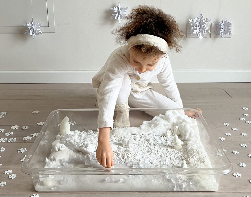 Bambina che gioca con un minimondo sensoriale artico sul colore bianco ispirato al Reggio Emilia Approach